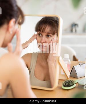 Middle-aged woman examining her facial skin looking in the mirror put on the table Stock Photo