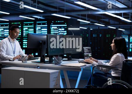 Person with disability and coworker in inclusive server room facility ensuring data remains shielded from threats. Wheelchair user and colleague protecting data center hardware equipment Stock Photo