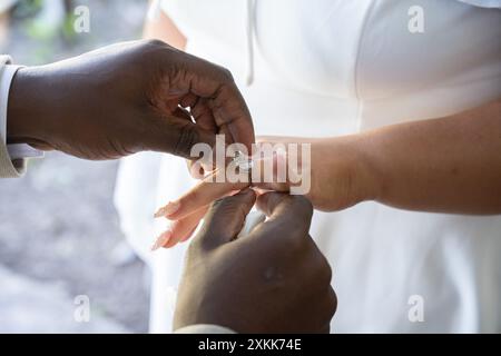 Black hands of the groom places wedding ring on the finger of his bride during ceremony. Stock Photo