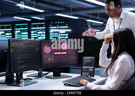 Computer scientist in server hub asking coworker for help, trying to protect equipment from hacker. IT specialist in data center facility requesting assistance to fix security breach alert Stock Photo