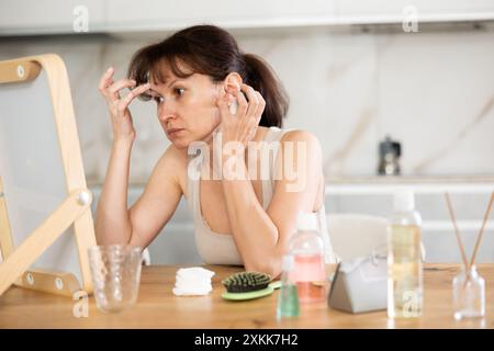 Middle-aged woman examining her facial skin looking in the mirror put on the table Stock Photo