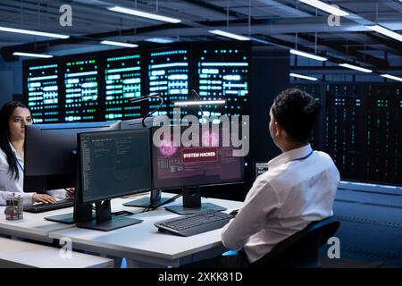 Teamworking developers in server room trying to protect hardware from cybercriminal attack. Data center cybersecurity division colleagues fighting malware during security breach Stock Photo