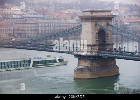 Riverboat passes under Chain Bridge built 1849 over Danube River - rebuilt in 1949 after WWII destruction - Budapest, Hungary - winter fog Stock Photo