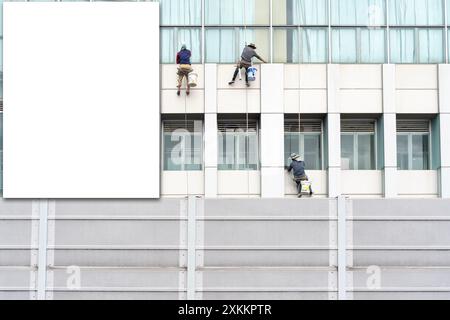 Blank poster on a building facade. Window washers at work. White empty signage on clothes shop front with glass windows. Stock Photo