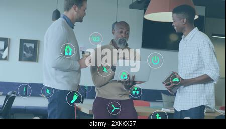Image of ecology icons over diverse colleagues using laptop and discussing work in office Stock Photo