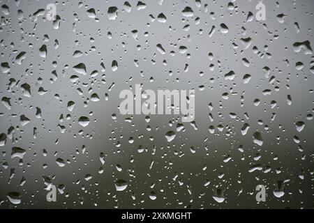 A window with raindrops on it. The raindrops are scattered all over the window, creating a blurry and hazy effect. Scene is calm and peaceful, as the Stock Photo