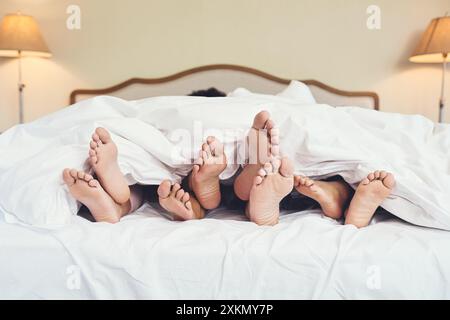 Bed, children and feet of parents in blanket with sleeping, resting and relax on holiday in hotel. Family, people and barefoot in sheets with weekend Stock Photo