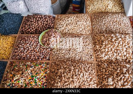 assortment of different variety nuts, dried fruits on counter at oriental food bazaar. Almonds, raisins, pistachios, hazelnuts, macadamia in market stall Stock Photo