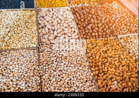 assortment of different variety nuts and dried fruits on counter at oriental bazaar. Almonds, raisins, pistachios, hazelnuts, macadamia in market stall Stock Photo