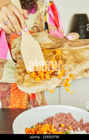 Close-up of a woman sprinkling sweet potatoes on a bowl with fresh minced meat, vegetables and herbs in the kitchen. Stock Photo