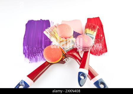 Three paintbrushes with red handles, each dipped in colorful paint, with matching macarons on a white background. Stock Photo