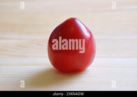 Closeup of a Fresh Dwarf Gulf Ruby Plum Isolated on Wooden Background Stock Photo