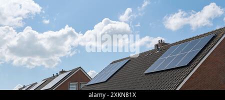 Blue solar cells or sun panels on roofs of houses in a row reflecting the blue cloudy sky. Green sustainable energy concept Stock Photo