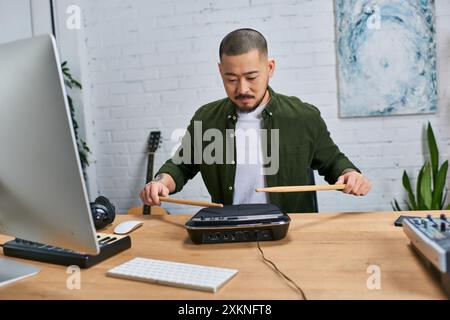 A young Asian man in a casual green shirt plays a drum pad in his studio. Stock Photo
