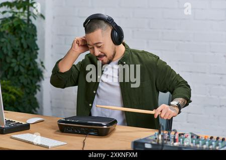 A young Asian man wearing headphones plays a drum pad in a recording studio. Stock Photo