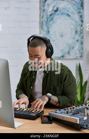 A young Asian man, wearing headphones, plays a keyboard in his studio. Stock Photo