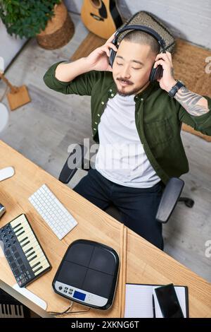 A young Asian man wearing headphones sits in a studio and plays musical instruments. Stock Photo