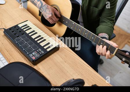A young Asian man plays an acoustic guitar and a MIDI keyboard in a studio setting. Stock Photo