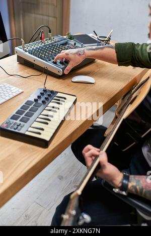 A young Asian man plays guitar and adjusts the soundboard in his studio. Stock Photo