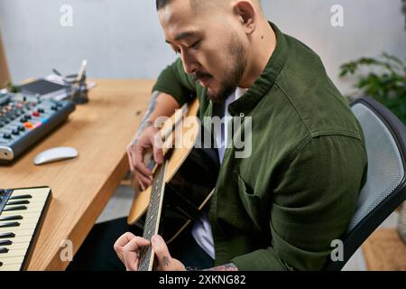 A young Asian man plays acoustic guitar in his studio. Stock Photo