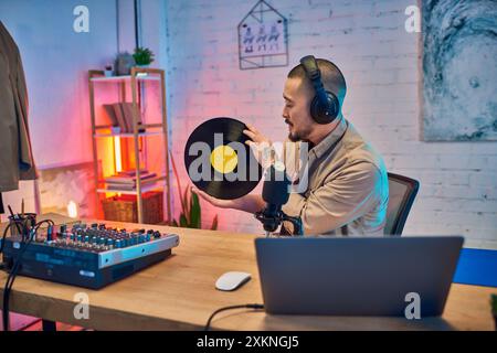 An Asian man with headphones listens intently to a vinyl record while recording a podcast. Stock Photo
