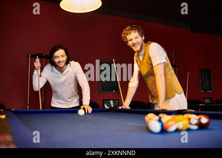 Two men in casual clothing play pool together in a dimly lit room. Stock Photo