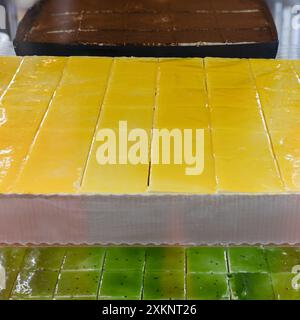 Yellow and Green Rectangular Cakes Cut into Square Slices and Displayed inside the Counter of a Pastry Shop. Stock Photo