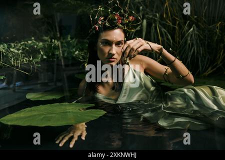 A woman wearing a floral crown and green dress poses in a swamp. Stock Photo