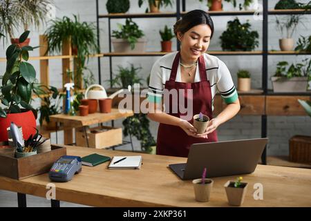 An Asian woman smiles warmly while holding a potted plant in her plant shop. Stock Photo