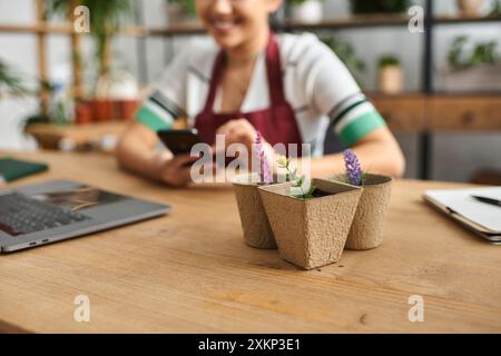 A smiling woman in an apron works in her plant store, using her phone to manage her small business. Stock Photo