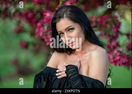 A woman in a black dress poses in front of a blooming pink tree. Shallow depth of feld Stock Photo