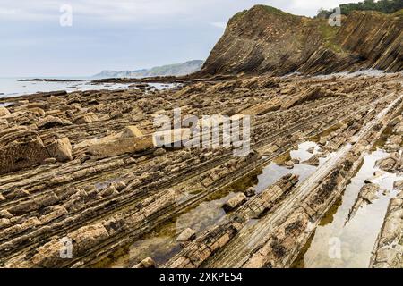 View of rock formations in horizontal layers of different materials with puddles of sea water. Sakoneta Flysch, Deba, Gipuzkoa, Basque Country, Spain. Stock Photo