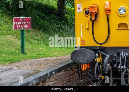 A beware of trains sign along side a stationary diesel train at the Watercress Line, Alresford, Hampshire, UK Stock Photo