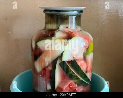 Jar of homemade pickled vegetables in brine, including watermelon and cucumber slices placed in a teal bowl Stock Photo