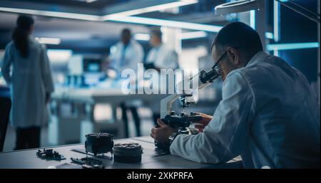 Scientist Using a Modern Digital Microscope in a Research and Development Facility. On Blurred Background Diverse Team of Industrial Specialists Working on Remotely Controlled Mobility Robot. Stock Photo