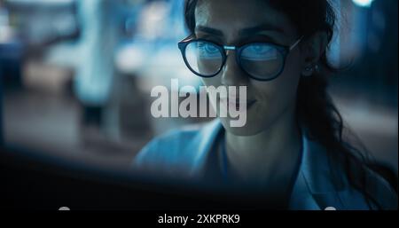 Portrait of Beautiful Multiethnic Woman Working on Computer with the Screen Reflecting in Her Glasses. Young Intelligent Female Scientist Working in Laboratory. Background with Technological Lights Stock Photo
