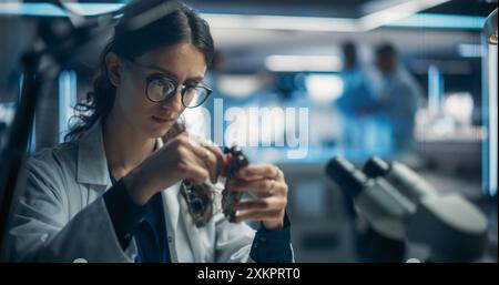 Focused Professional Female Engineer Working on Electronic Circuit Boards. Industrial Robotics Specialists in Laboratory Coats Developing Mobile AI Robot in an Advanced Technology Factory Facility. Stock Photo