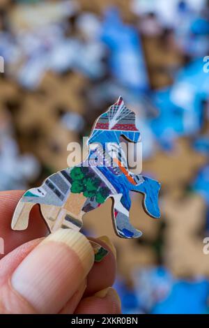 Hand holding Wentworth whimsy piece jigsaw puzzle piece above box of Wentworth Wooden Puzzles puzzle pieces Stock Photo