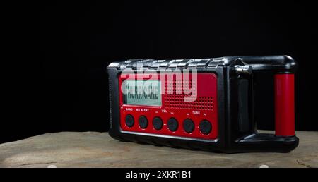 Red battery powered weather radio with a hurricane warning diplayed on its LCD screen with a black background and copy space. Stock Photo