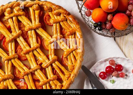 Apricot pie decorated with dough ornament and a metal basket with fruits and berries on a light background. Rustic style, selective focus. Stock Photo