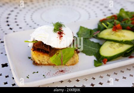 Healthy poached egg dressed with fresh dill on top of potatoe kugel on white plate on patio table Stock Photo