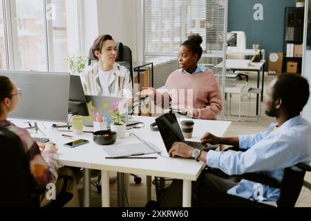 Biracial colleagues discussing next goals while sitting at white table in modern IT company office equipped with electronic devices Stock Photo