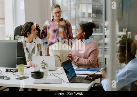Biracial colleagues chatting in office while their african american coworker using laptop to write codes Stock Photo