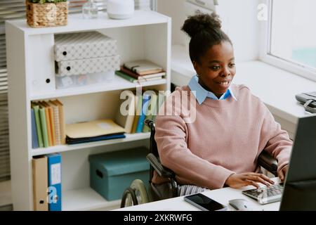 Young African American female programmer with disability enjoying coding in cozy light office of modern IT company Stock Photo