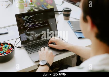 Over shoulder shot of unrecognizable male IT specialist typing on keyboard while computer screen showing code Stock Photo