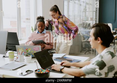 Biracial female coworkers having discussion and looking at touchpad while male programmer writing codes Stock Photo