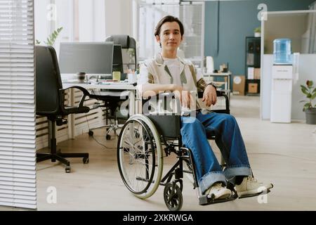 Portrait of modest highly experienced programmer with disability sitting for photo in center of modern office fully equipped with electronic devices a Stock Photo