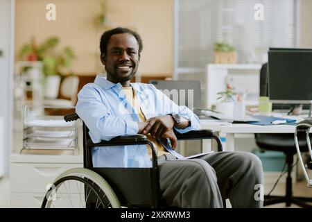 Smiling African American developer in wheelchair in cozy and light office of huge successful IT company Stock Photo