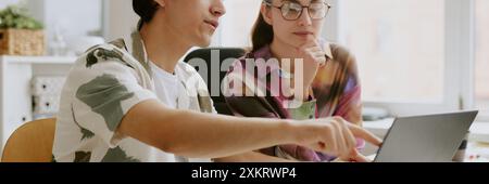 Website header shot of two coworkers sitting at table desk and looking at laptop screen in office Stock Photo