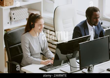 Male and female coworkers typing on black keyboard and looking at huge monitor while sitting at their workplaces in modern office Stock Photo